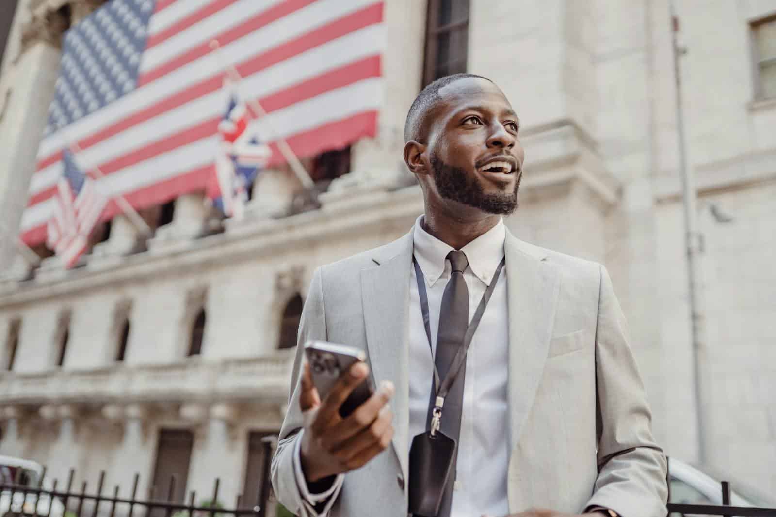 Confident businessman using smartphone in front of iconic building with American flags.