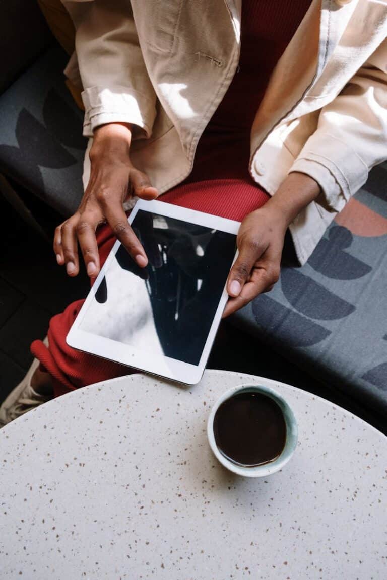 An adult woman using a tablet in a cozy café setting with a cup of coffee.