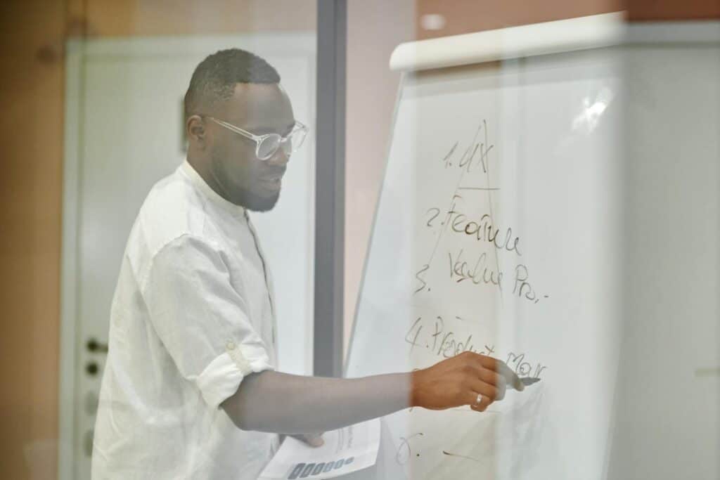 Professional man presenting business strategy on a whiteboard in a modern office setting.